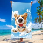 Ręcznik plażowy 100x180 cm z mikrofibry, przedstawiający uśmiechniętego pieska na niebieskim tle z chmurami. Produkt trzymany przez osobę na plaży, w tle morze i palmy. Szybkoschnący materiał, duży rozmiar, idealny na wakacje.