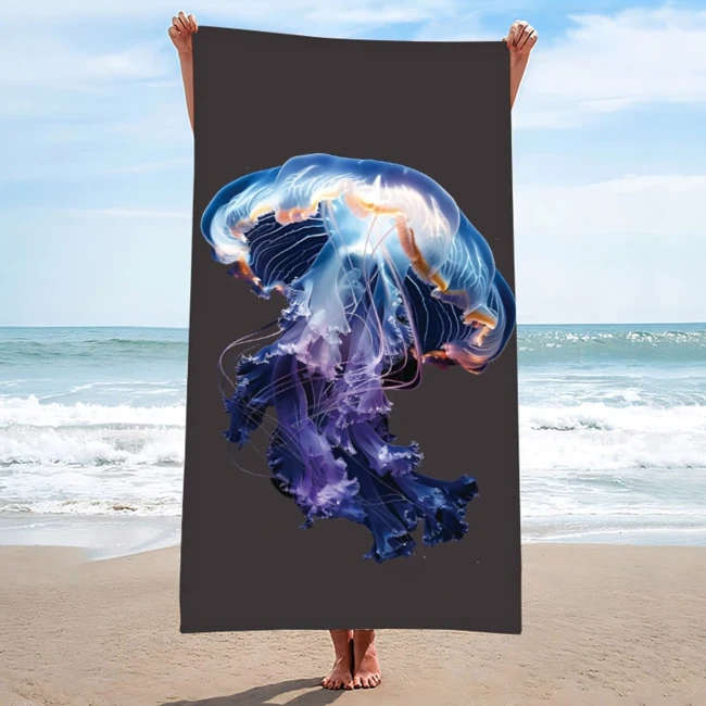 Ręcznik plażowy 100x180 cm, wykonany z mikrofibry, z grafiką przedstawiającą meduzę w kolorze niebiesko-fioletowym na ciemnym tle. Produkt trzymany w pionie, z plażą i morzem w tle, idealny do użytku w sezonie letnim.