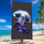 Duży ręcznik plażowy z mikrofibry o wymiarach 100x180 cm, przedstawiający realistyczny wzór meduzy w odcieniach niebieskiego i fioletowego na ciemnym tle. Ujęcie frontalne, ręcznik trzymany przez osobę stojącą na plaży, w tle morze i palmy.