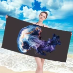 Ręcznik plażowy 100x180 cm z mikrofibry, z wydrukiem meduzy w odcieniach niebieskiego i fioletowego. Produkt trzymany w pozycji pionowej przez modelkę na tle plaży, z jasnym niebem i morzem. Idealny do użytku na plaży lub basenie.