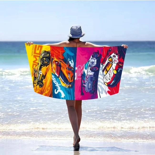 Ręcznik plażowy 100x180 cm z mikrofibry w sportowe auta. Kolorowe wzory przedstawiają różne samochody na tle błękitu. Produkt trzymany przez osobę na plaży, z widokiem na morze, rozłożony, aby pokazać jego atrakcyjny design i wielkość.