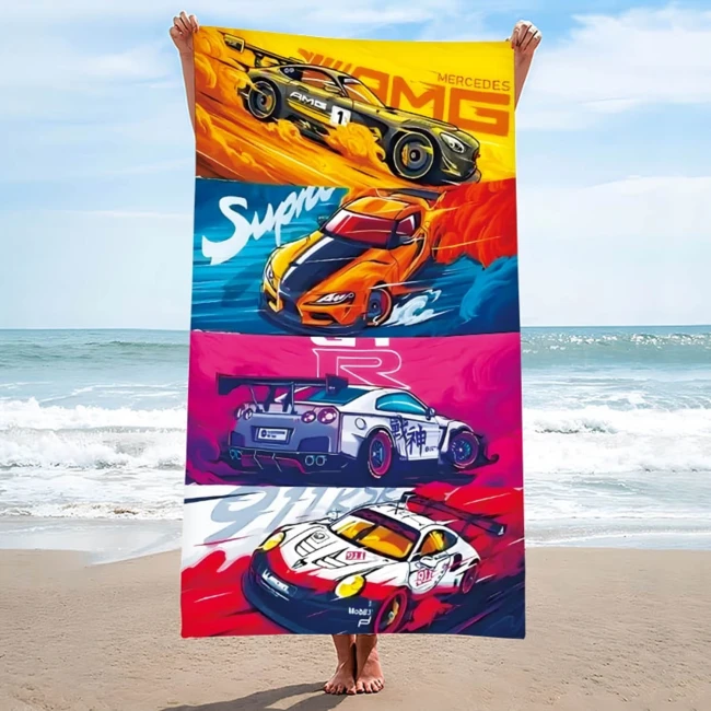 Ręcznik plażowy 100x180 cm z mikrofibry z grafiką sportowych aut. Widoczny z przodu, trzymany przez osobę na plaży.