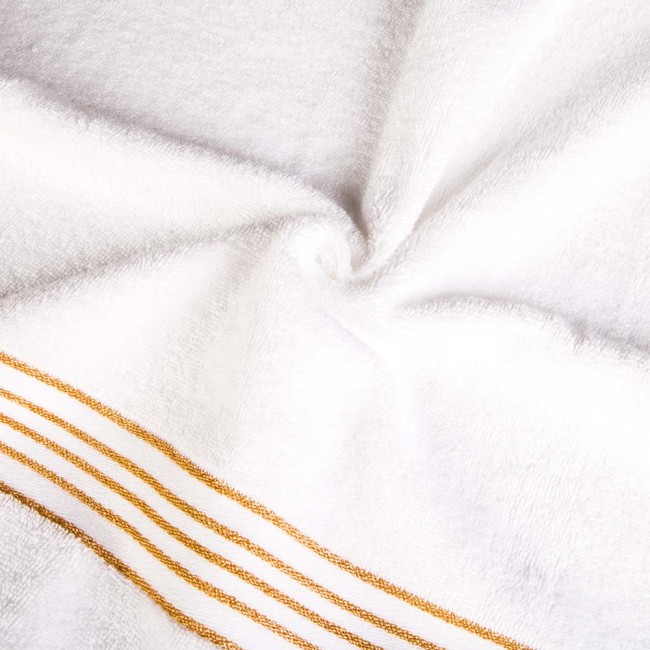 Ręcznik do rąk o wymiarach 30x50 cm, wykonany z białej bawełny z bordiurą w złote paski. Widać teksturę materiału i delikatne wytłoczenie. Produkt złożony, ułożony na tle o neutralnym, jasnym kolorze.