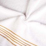 Biały ręcznik kąpielowy 50x90 cm z bawełny, 500 g/m², z bordiurą w złote paski. Ułożony w zrolowany sposób, ukazujący teksturę materiału i detale zdobienia. Proste, jasne tło podkreśla elegancję produktu.