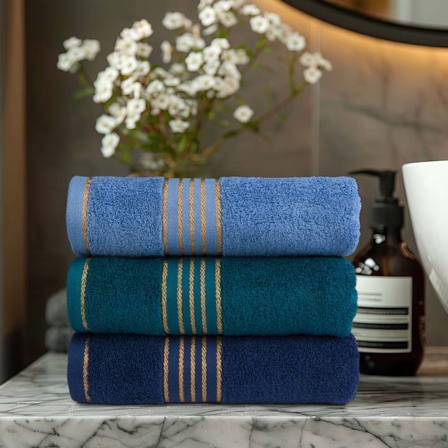 Ręcznik do rąk 30x50 cm w kolorze ciemnym niebieskim, z bordiurą w złote paski. Ułożony poziomo, w zbliżeniu, na marmurowym blacie. W tle widoczne akcesoria łazienkowe oraz kwiaty, co podkreśla nowoczesny wygląd przestrzeni.