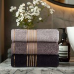 Ręcznik do rąk 30x50 cm w kolorze ciemnego szarego z bordiurą w złote paski, ułożony w pionie. Produkt bawełniany o gramaturze 500 g/m², widoczny na marmurowym blacie w aranżacji z elementami łazienkowymi. Trzy warianty ręczników obok siebie.