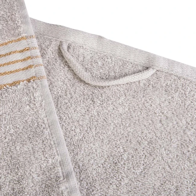 Ręcznik kąpielowy bawełniany o wymiarach 50x90 cm w jasnym szarym kolorze, z bordiurą w złote paski. Złożony, z widocznym detalem pętli do powieszenia. Tekstura materiału jest miękka i chłonna, idealna do stosowania po kąpieli.