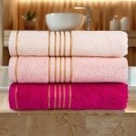 Ręcznik do rąk 30x50 cm w jasnym różowym kolorze z bordiurą w złote paski, wykonany z bawełny o gramaturze 500 g/m2. Ręczniki ułożone poziomo na blacie, z widocznym miękkim splotem i detali złotych pasków. Tło stanowi stylowe wnętrze łazienki.
