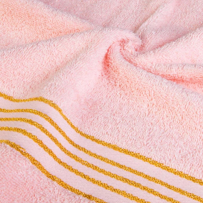 Ręcznik kąpielowy 50x90 cm w jasnym różowym kolorze, wykonany z bawełny o gramaturze 500 g/m2. Widoczne złote paski wzdłuż bordiury, miękka, teksturowana powierzchnia, złożony w płaskiej pozycji na jednolitym tle.