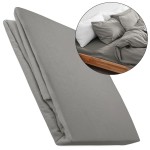 Flanelowe prześcieradło z gumką w kolorze szarym, wykonane z materiału 160g/m², leży złożone na białym tle. Na zdjęciu widoczny fragment prześcieradła z wyraźną fakturą; w tle zarys łóżka z pościelą w odcieniach szarości.