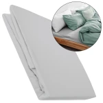 Prześcieradło flanelowe z gumką 120x200 w jasno szarym kolorze, wykonane z materiału o gramaturze 160g/m². Produkt leży na płaskiej powierzchni, zwinięty, ukazując jego teksturę. W tle widoczne poduszki i kołdra w różnych kolorach.