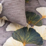 Pościel flanelowa 180x200 cm Solenne Dark w odcieniach szarości i bieli z motywem liści miłorzębu. Ułożona na płasko, z widocznymi poduszkami. Tło w kolorze jasnoszarym z drobnym wzorem, podkreślającym dekoracyjne, zielono-żółte liście.