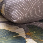 Pościel flanelowa 180x200 cm w kolorze ciemnoszarym, z wzorem liści miłorzębu w odcieniach zieleni i żółci. Ułożona na tle, zbliżenie na detal, poduszka wyraźnie wyeksponowana z białymi kropkami na materiale. Tekstura flaneli, matowe wykończenie.