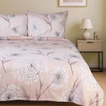 Pościel flanelowa 140x200 cm Aureli Beige w delikatny wzór dmuchawców na beżowym tle. Złożona, z poduszkami widocznymi z góry. Oświetlenie ciepłe, otoczenie przytulne z nocną lampką i drewnianą szafką obok.