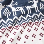 Pościel flanelowa 180x200 w bordowym kolorze z wzorem reniferów i krateczką, wykonana z miękkiego materiału. Ułożona w sposób lekko złożony, eksponuje detale graficzne. Wzór kontrastuje z białym tłem.