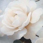 Kościej na pościel satynową w kolorze szarym z kremowymi różami. Wzór kwiatu widoczny w zbliżeniu na dużą różę z delikatnymi płatkami. Tło w jasnych odcieniach, co podkreśla detale roślinne. Produkt rozłożony, odpowiedni do aranżacji sypialni.