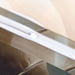 Zamek błyskawiczny pościeli satynowej w kremowe róże, widoczny na zdjęciu, jest biały. W tle delikatne kolory tkaniny, co podkreśla wzór kwiatowy. Produkt leży płasko, ukazując detal zapięcia oraz fakturę materiału.