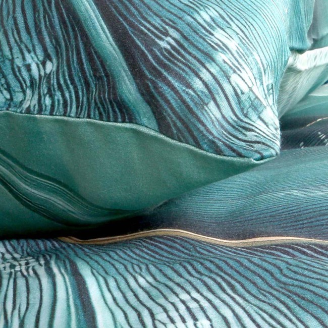 Pościel satyna bawełniana 140x200 w zielonym kolorze z wzorem w liście, z detalami w złotym odcieniu. Zbliżenie na materiał o gładkiej, błyszczącej fakturze, z widocznymi napami w złotym kolorze.