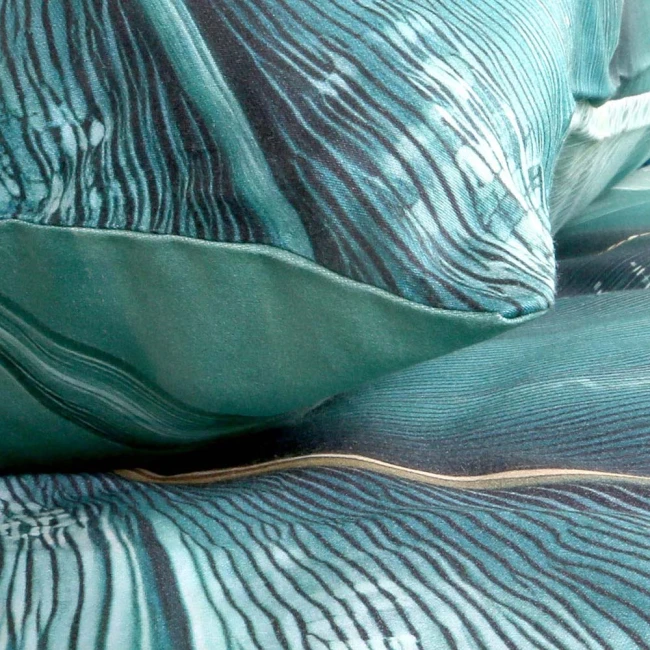 Pościel satyna bawełniana 160x200 w odcieniu zieleni z wzorem liści i złotymi akcentami. Ułożona w sposób zwinięty, z widocznymi detalami materiału oraz faktury. Tło jest jasne, co podkreśla kolorystykę poszwy i poduszek.
