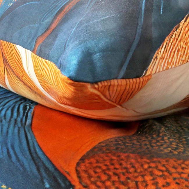 Poduszka z pościeli satynowej, kolorowa, z motywem złotych i niebieskich liści. Widoczna tekstura materiału. Ujęcie z bliska, ukazujące szczegóły wzoru. Produkt leży na płaskiej powierzchni, podkreślając jego rozmiar 180x200 cm.