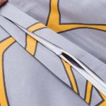 Zbliżenie na zamek błyskawiczny pościeli w kolorze szarym z pomarańczowym wzorem liści. Widoczne elementy materiału o satynowej fakturze, zamknięty zamek w kolorze białym, który umożliwia łatwe wsunięcie poduszki i kołdry.