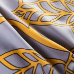 Pościel satyna bawełniana 220x200 Folina w pomarańczowe liście na szarym tle, ukazana z bliska. Wzór z liśćmi w intensywnym odcieniu pomarańczowym na matowej, szarej tkaninie. Widoczna gładka faktura materiału.