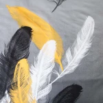 Pościel satyna bawełniana 140x200 w kolorze szarym z wzorem białych, czarnych i złotych piór. Produkt leży na płaskiej powierzchni, prezentując detale nadrukowanych piór na gładkim tle.