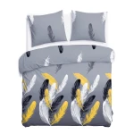 Pościel satyna bawełniana 180x200 Fevola w białe, złote i czarne pióra na szarym tle. W komplecie poszewki na poduszki. Produkt leży rozłożony, ukazując detale wzoru i fakturę materiału. Tło jest jednolite, co podkreśla kolorystykę pościeli.