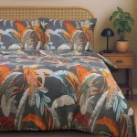Pościel satynowa 140x200 w tropikalne liście na szarym tle, ułożona na łóżku. Widoczne dwie poszewki na poduszki oraz prześcieradło z żywymi kolorami liści w odcieniach pomarańczowym, niebieskim i zielonym.