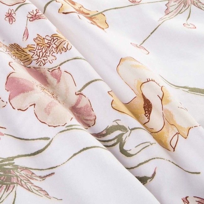 Pościel satyna bawełniana 140x200 Floralis w delikatne kremowe kwiaty na białym tle, leżąca w złożeniu. Wzór obejmuje pastelowe odcienie różu i żółci, z widocznymi detalami kwiatów. Tło jest jasne i jednolite, co podkreśla wzory.