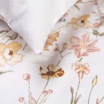 Pościel satyna bawełniana 140x200 w delikatny kremowy wzór kwiatowy na białym tle. Poduszka leżąca na pościeli. Widoczne detale w postaci kwiatów w odcieniach różu i żółci, z teksturą gładkiej satyny.