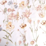 Pościel z satyny bawełnianej 140x200 z delikatnym kremowym wzorem kwiatów na białym tle. Ułożona na płasko, z widocznymi szczegółami roślinności, w tym lilii, maków i innych drobnych kwiatów. Tło jest jednolite, co podkreśla kolorystykę.