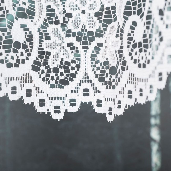 Firana gotowa BERENIKA żakardowa, w kolorze białym, z subtelnym wzorem. Zbliżenie na dolną krawędź, ukazującą koronkowe zdobienia. Materiał lekki, teksturowany, idealny do okna. Tło w odcieniach szarości, minimalistyczne. Wymiary 400x160 cm.