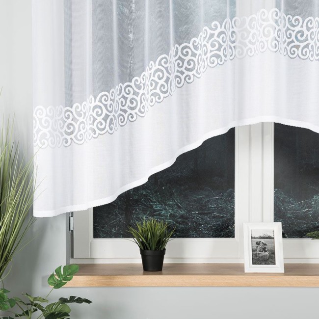 Firana gotowa DANIELA żakardowa, biała, o wymiarach 300x140 cm, zawieszona na oknie. W dolnej części widoczna dekoracyjna haftowana bordiura.
