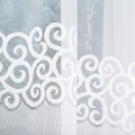 Biała firana gotowa DANIELA z żakardowym wzorem, o szerokości 300 cm i wysokości 140 cm, wisząca na oknie. Wzór z falistymi spiralami jest wpleciony w tkaninę, podkreślający jej teksturę i przezroczystość. Tło minimalistyczne.