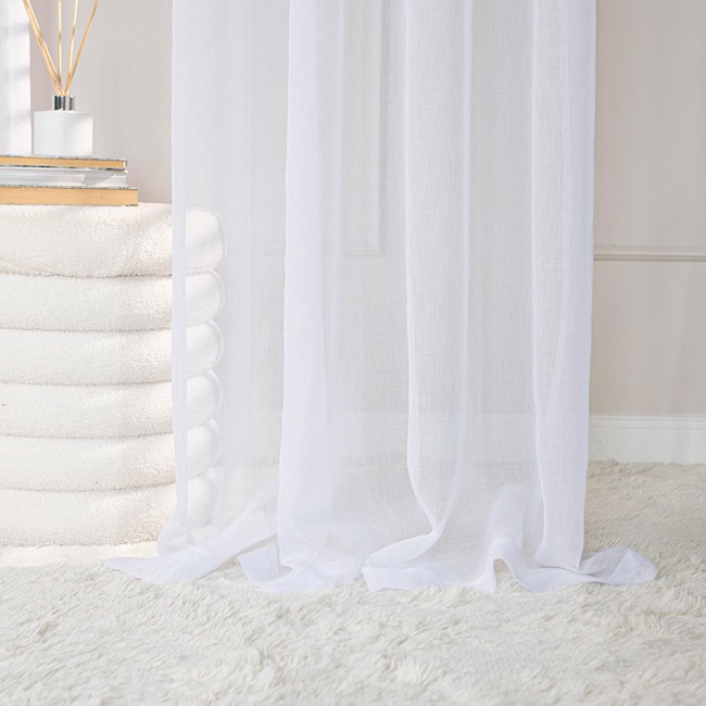 Firana gotowa ETAMINA na srebrnych przelotkach, biała, o wymiarach 200x250 cm, zwisająca pionowo na białym tle z meblami. Tkanina jest lekka i transparentna, idealna do wprowadzenia naturalnego światła do wnętrza. Srebrne przelotki ułatwiają zawieszenie.