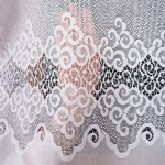 Firana żakardowa MODESTA w kolorze białym, o wymiarach 200x250 cm. Widoczna finezyjna siateczka z wzorem w formie spiralnych zdobień oraz falistym wykończeniem. Produkt rozłożony, zbliżenie na detal faktury tkaniny.