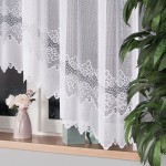 Firana żakardowa MODESTA w kolorze białym, o wymiarach 300x160 cm, zawieszona w oknie. Zbliżenie na fakturę materiału z delikatnym wzorem w dolnej części. W tle widoczna doniczka z kwiatami i elementy dekoracyjne na parapecie.