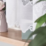 Firana gotowa MODESTA żakardowa w kolorze białym, o rozmiarze 300x160 cm, wisząca na oknie. Wzór z delikatnymi falami i ornamentami. W tle widoczny różowy wazon z kwiatami oraz zielona skrzynka, stanowiąca część aranżacji okna.