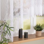 Firana materiałowa MODESTA, żakardowa, w kolorze białym, o wymiarach 400x160 cm, zawieszona w oknie. Kąt ujęcia frontalny, zbliżony na dolną krawędź firany, ukazujący dekoracyjny, falbaniasty wzór.