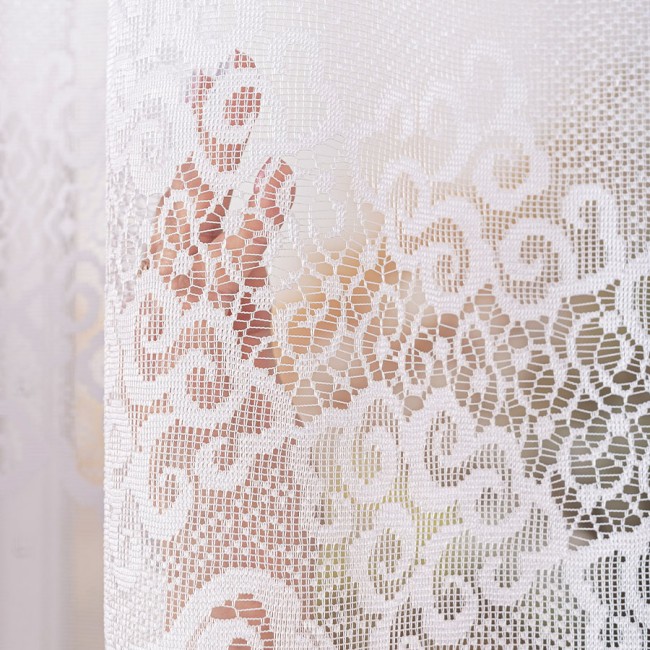 Firana gotowa MODESTA żakardowa, biała, o wymiarach 400x160 cm, w formie zwisającego panelu. Wzór z delikatnymi motywami roślinnymi, widoczna tekstura materiału. Ujęcie zbliżeniowe, ukazujące szczegóły splotu na tle rozmytego otoczenia.