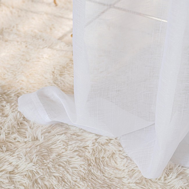 Firana gotowa NALA na przelotkach, biały materiał o gładkiej fakturze, prezentująca się w opadającej pozycji na jasnozłotej podłodze. Widoczna część przelotki, podkreślająca sposób zawieszenia. Tło intensywnie neutralne.