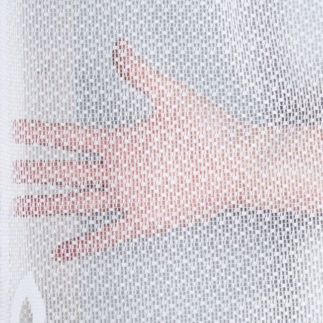 Firana gotowa POLA żakardowa, biała, o wymiarach 300x160 cm. Zbliżenie na fakturę materiału, widoczna ręka za firaną. Przezroczysty wzór pozwala na delikatne przepuszczanie światła. Produkt wiszący, na jednolitym tle.