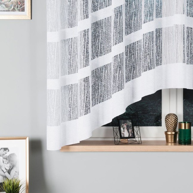 Firana gotowa WIKTORIA, żakardowa, biała, o wymiarach 310x160 cm. Zawieszona, z delikatnym, wzorzystym splotem. W tle widoczna drewniana półka z dekoracjami oraz neutralne, szare ściany, które podkreślają jasność firany.