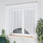 Firana gotowa ZUZANNA, biała, żakardowa, wzór po całości z roślinnością. Zawieszona na karniszu w oknie, z widocznym detalem falbanek na dolnej krawędzi. W tle delikatne światło dzienne, obok doniczka z roślina. Wymiary: 300x160 cm.