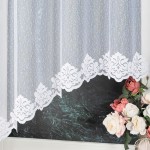 Firana żakardowa w kolorze białym z dekoracyjnym, koronowym wykończeniem u dołu. Rozmiar 330x160 cm, zawieszona w oknie. Przezroczysta tkanina z delikatnym wzorem, w tle widoczne ciemne otoczenie oraz bukiet różowych kwiatów.
