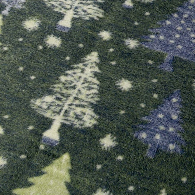 Dwustronny koc bawełniany 150x200 cm w zielonym kolorze z wzorem choinek i gwiazdek. Faktura jest miękka i teksturowana. Zdjęcie w zbliżeniu, ukazujące detale wzoru na kocu. Frędzle widoczne na brzegach. Brzegi wzmocnione, bez tekstu czy logo.