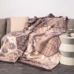 Koc bawełniany 150x200 cm w mozaikowym wzorze w odcieniach beżowym i brązowym, dwustronny, z frędzlami. Rozłożony na sofie, obok poduszka w jasnym kolorze. Widoczny detal struktury tkaniny oraz frędzli przy krawędzi.