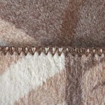 Koc bawełniany dwustronny w kolorze beżowo-brązowym o wymiarach 150x200 cm, widoczny w zbliżeniu na detale ściegu. Produkt posiada frędzle, a jego faktura jest miękka i przyjemna w dotyku.