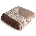 Dwustronny koc bawełniany w rozmiarze 150x200 cm, w odcieniach beżowym i brązowym, z dekoracyjnymi frędzlami na jednym z brzegów. Wzór mozaikowy, leżący w pozycji złożonej, umieszczony na białym tle, eksponujący fakturę materiału.
